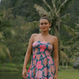 woman with brown hair wearing a navy strapless mini dress with ruffle hem and bright pink hibiscus print