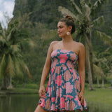 woman with brown hair wearing a navy strapless mini dress with ruffle hem and bright pink hibiscus print