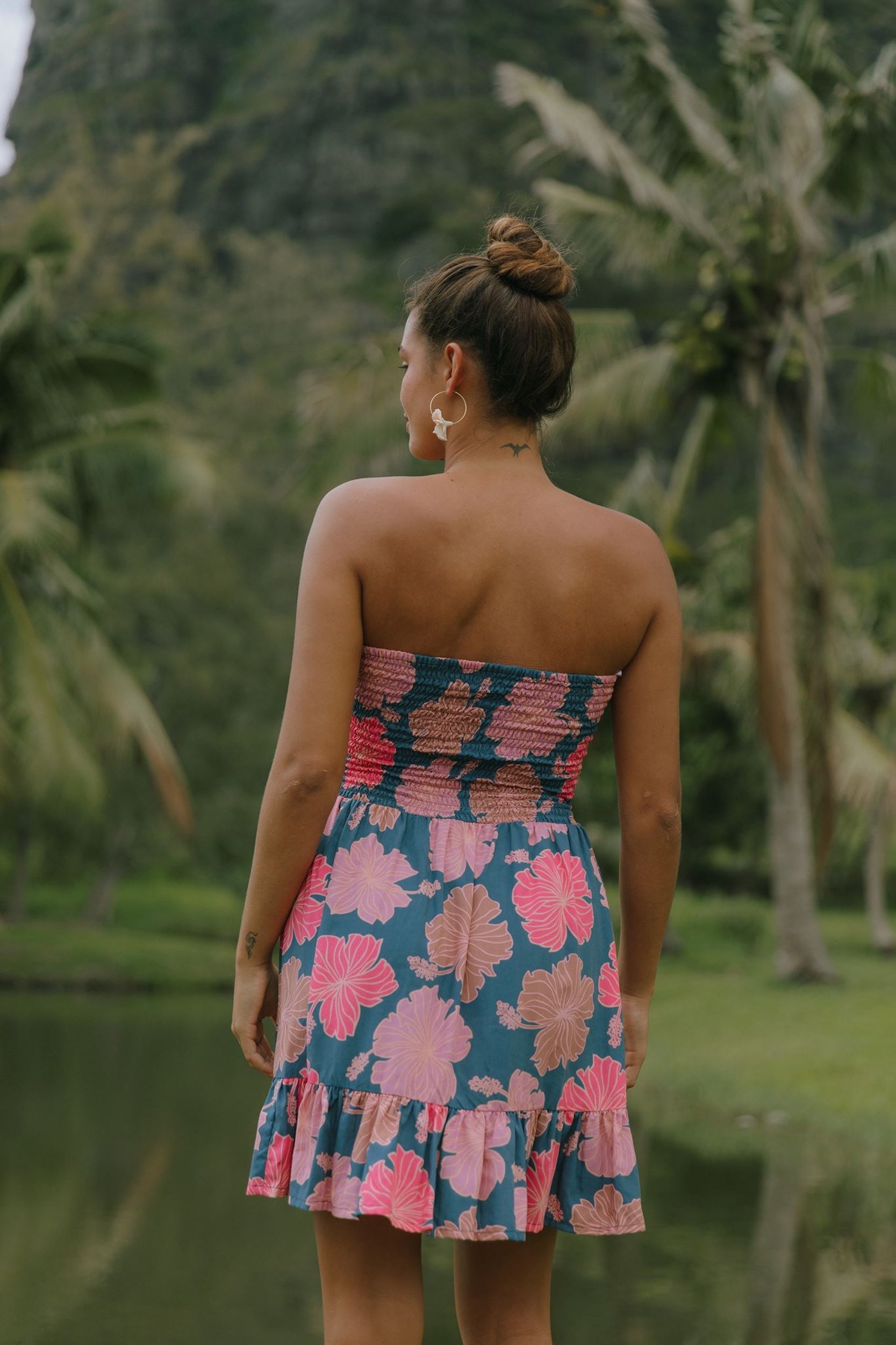 woman with brown hair wearing a navy strapless mini dress with ruffle hem and bright pink hibiscus print