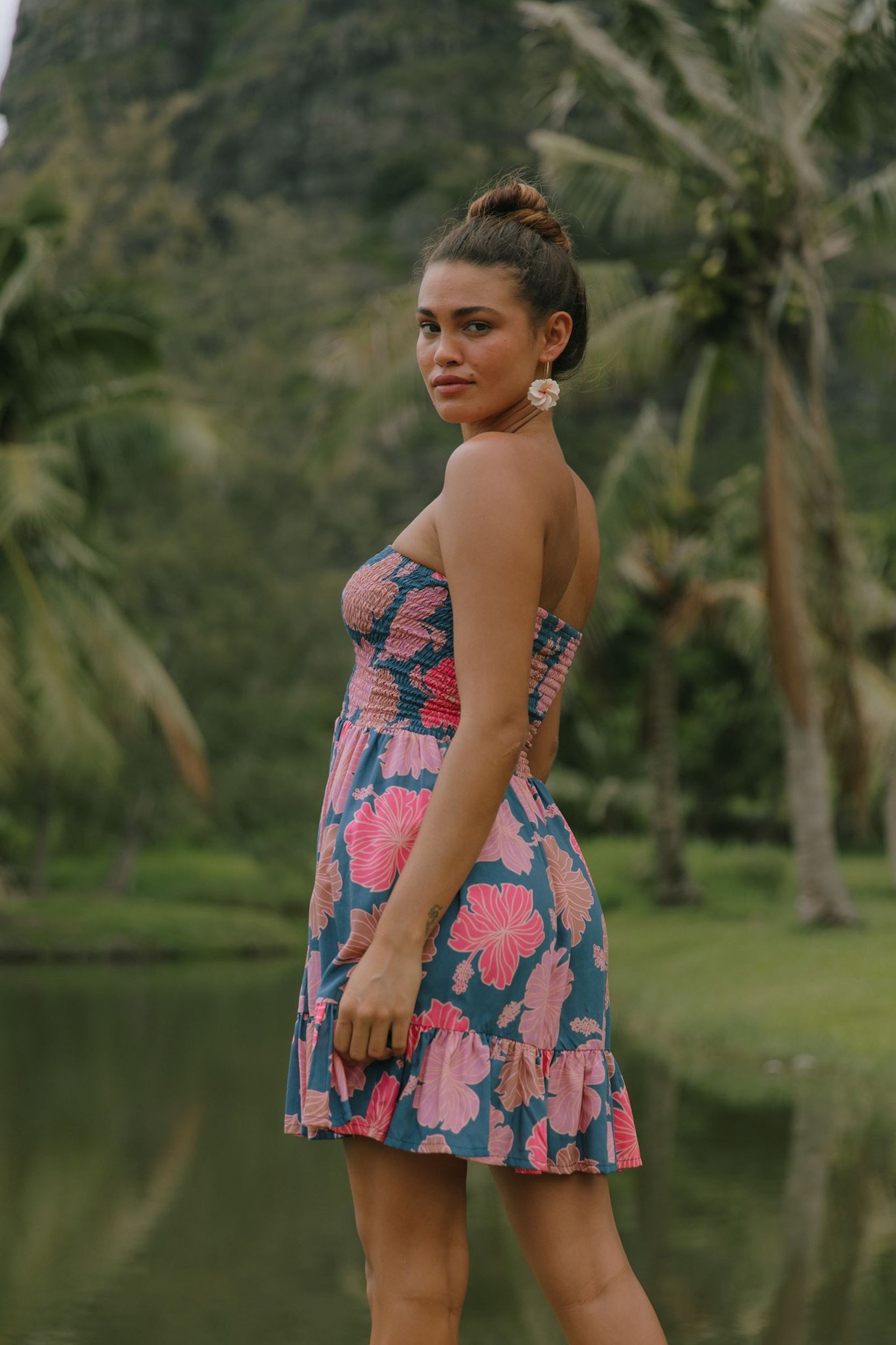 woman with brown hair wearing a navy strapless mini dress with ruffle hem and bright pink hibiscus print