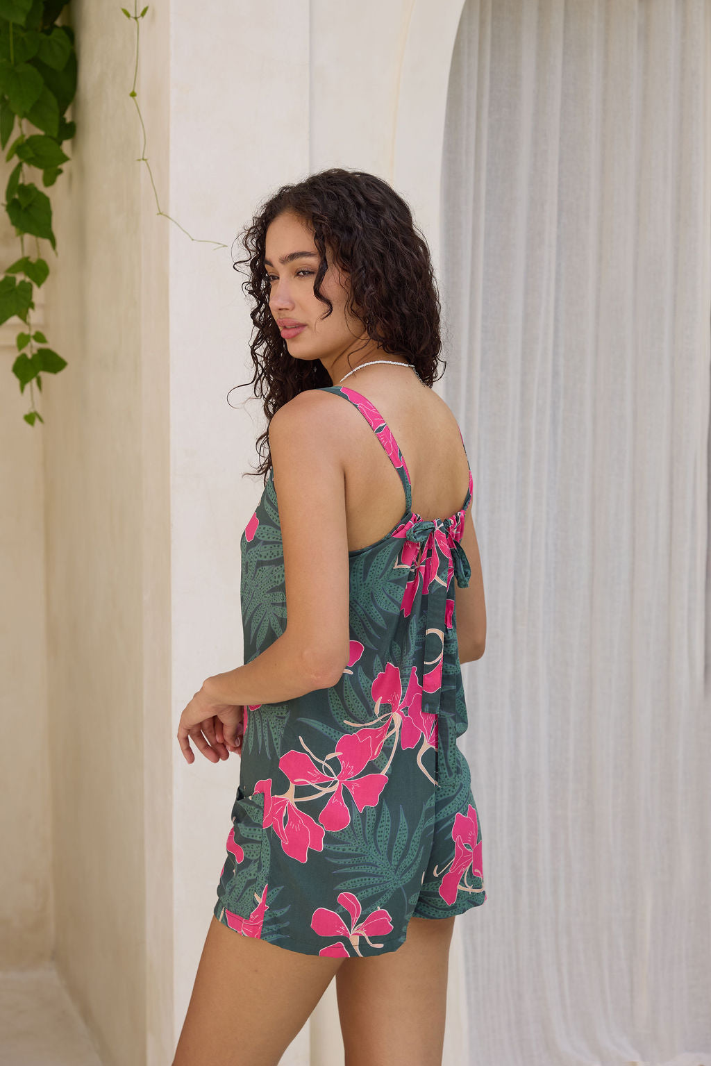 woman with brown hair wearing dark green tie back romper with fern and ginger print