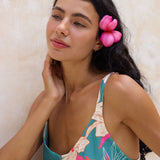woman with brown hair wearing a romper in teal with large cream colored orchids.