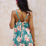 woman with brown hair wearing a romper in teal with large cream colored orchids.