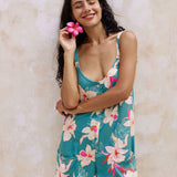 woman with brown hair wearing a romper in teal with large cream colored orchids.