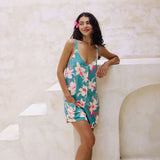 woman with brown hair wearing a romper in teal with large cream colored orchids.