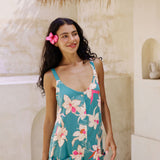 woman with brown hair wearing a romper in teal with large cream colored orchids.