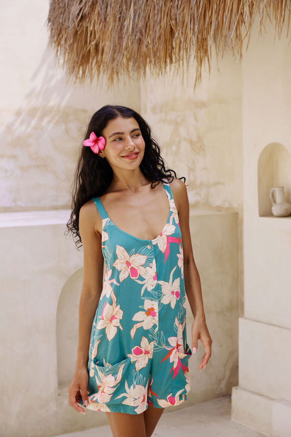 woman with brown hair wearing a romper in teal with large cream colored orchids.