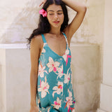 woman with brown hair wearing a romper in teal with large cream colored orchids.
