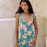 woman with brown hair wearing a romper in teal with large cream colored orchids.