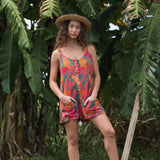 woman with brown hair wearing a colorful romper with tropical lei print