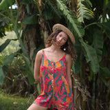 woman with brown hair wearing a colorful romper with tropical lei print
