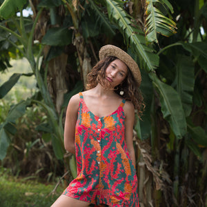 woman with brown hair wearing a colorful romper with tropical lei print