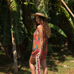 woman with brown hair wearing a colorful romper with tropical lei print