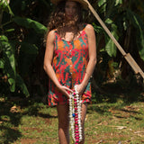 woman with brown hair wearing a colorful romper with tropical lei print