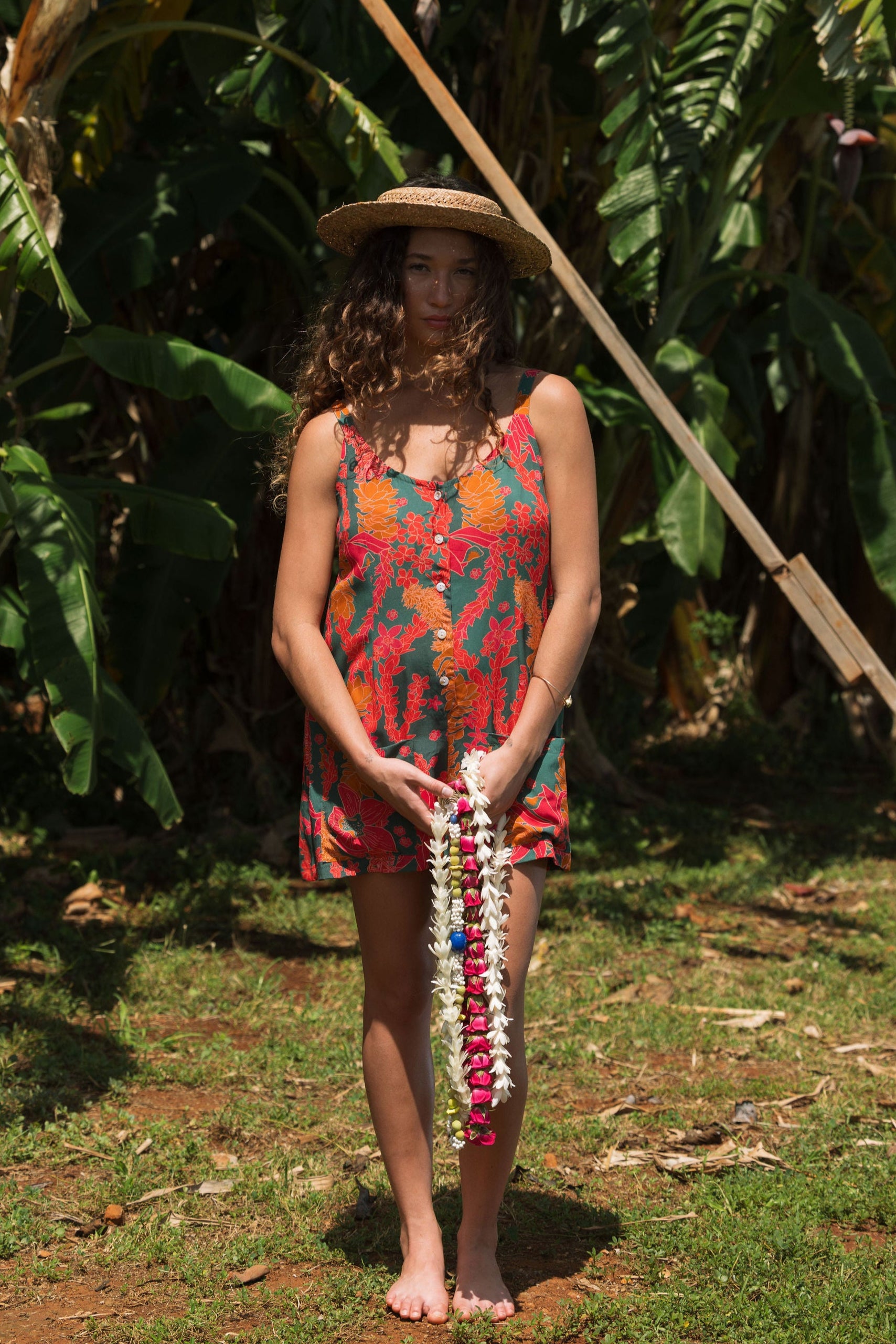 woman with brown hair wearing a colorful romper with tropical lei print