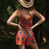 woman with brown hair wearing a colorful romper with tropical lei print