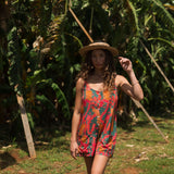 woman with brown hair wearing a colorful romper with tropical lei print