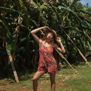 woman with brown hair wearing a colorful romper with tropical lei print