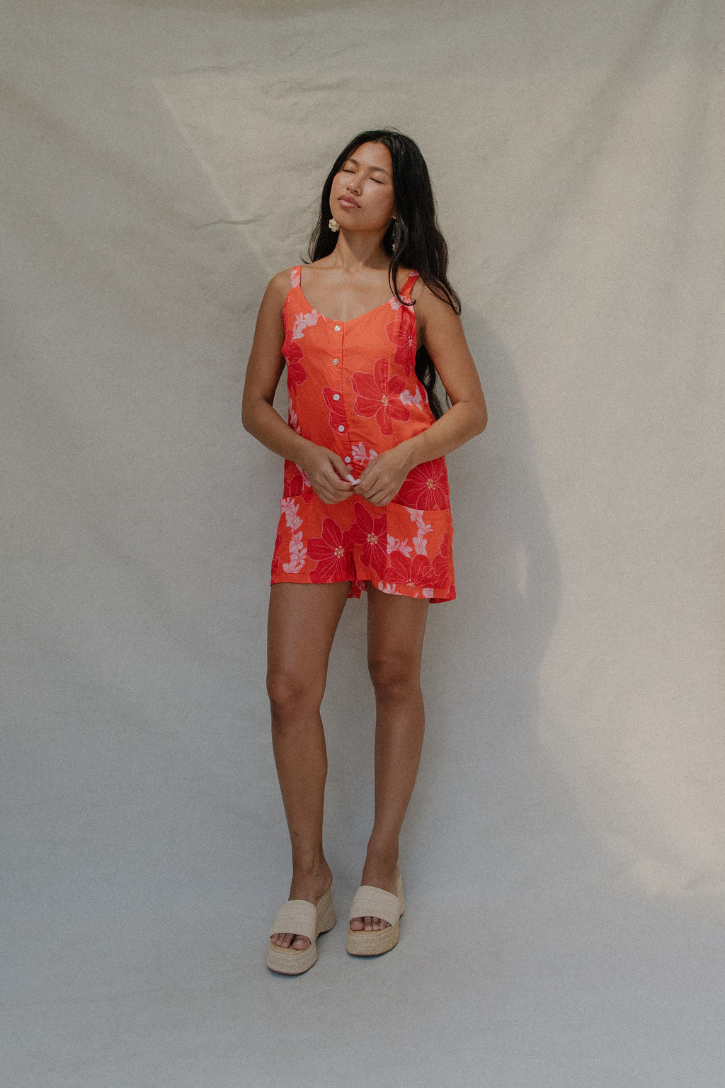 woman with brown hair a bright retro orange romper with a tie back detail and flower pattern
