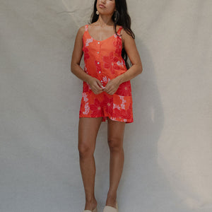woman with brown hair a bright retro orange romper with a tie back detail and flower pattern