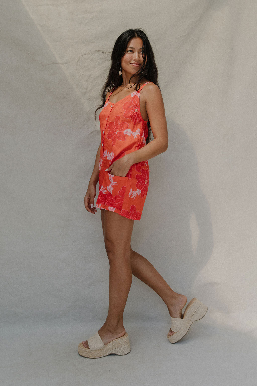 woman with brown hair a bright retro orange romper with a tie back detail and flower pattern