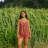 woman with brown hair wearing a red-brown colored romper with buttons, a tie back, front pockets, and lei print