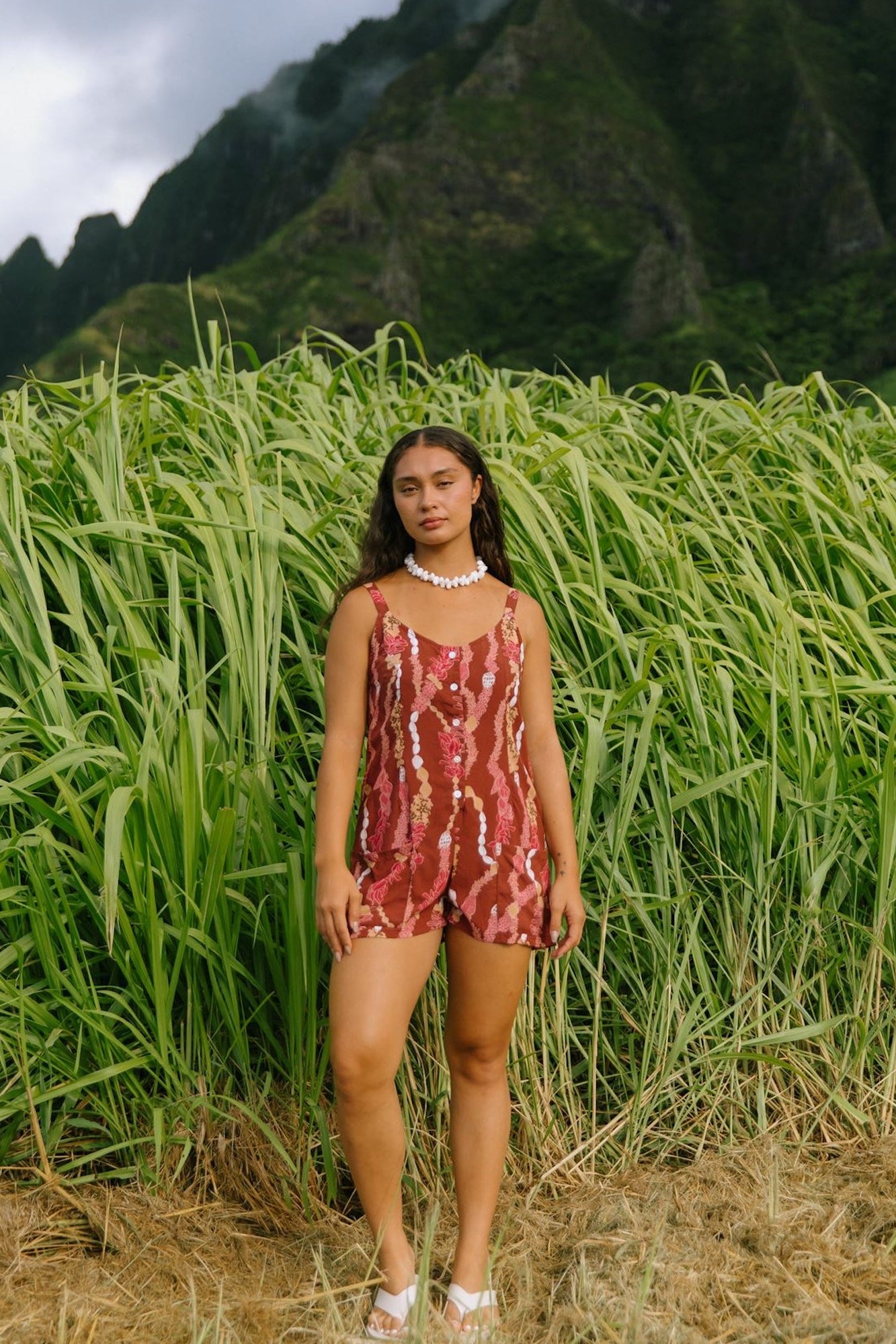 woman with brown hair wearing a red-brown colored romper with buttons, a tie back, front pockets, and lei print