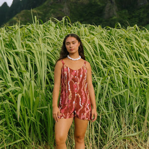 woman with brown hair wearing a red-brown colored romper with buttons, a tie back, front pockets, and lei print