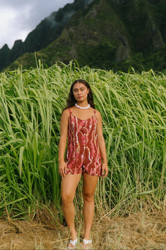woman with brown hair wearing a red-brown colored romper with buttons, a tie back, front pockets, and lei print