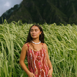 woman with brown hair wearing a red-brown colored romper with buttons, a tie back, front pockets, and lei print