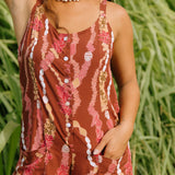 woman with brown hair wearing a red-brown colored romper with buttons, a tie back, front pockets, and lei print