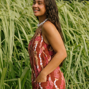 woman with brown hair wearing a red-brown colored romper with buttons, a tie back, front pockets, and lei print