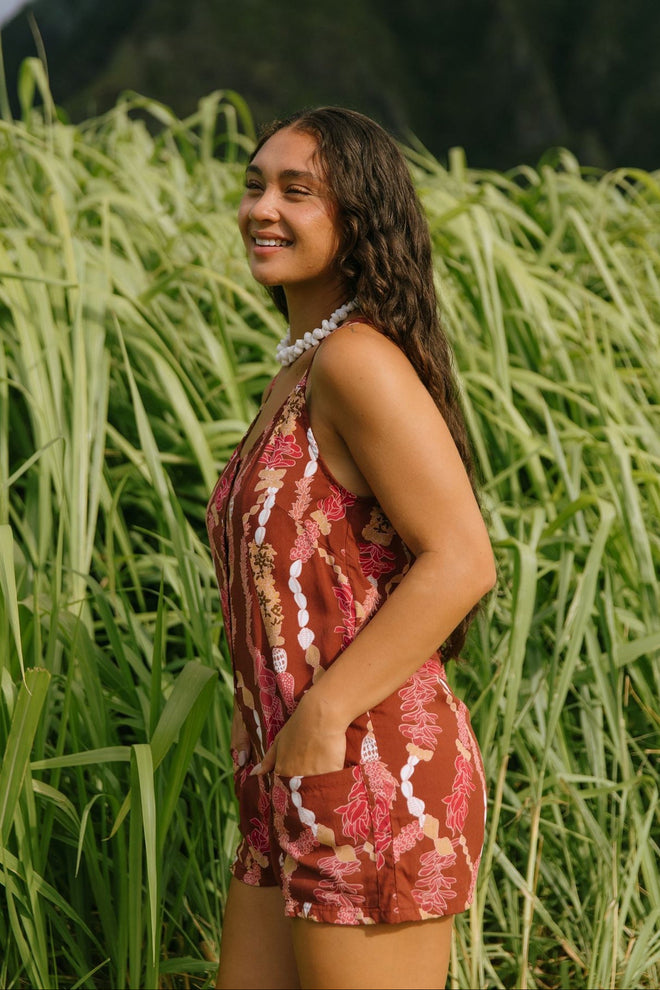 woman with brown hair wearing a red-brown colored romper with buttons, a tie back, front pockets, and lei print