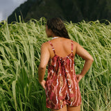 woman with brown hair wearing a red-brown colored romper with buttons, a tie back, front pockets, and lei print