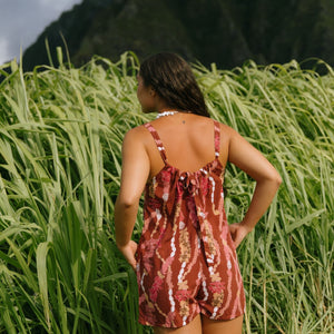 woman with brown hair wearing a red-brown colored romper with buttons, a tie back, front pockets, and lei print