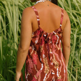 woman with brown hair wearing a red-brown colored romper with buttons, a tie back, front pockets, and lei print