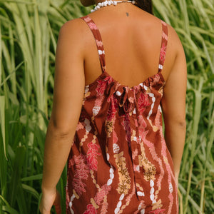 woman with brown hair wearing a red-brown colored romper with buttons, a tie back, front pockets, and lei print