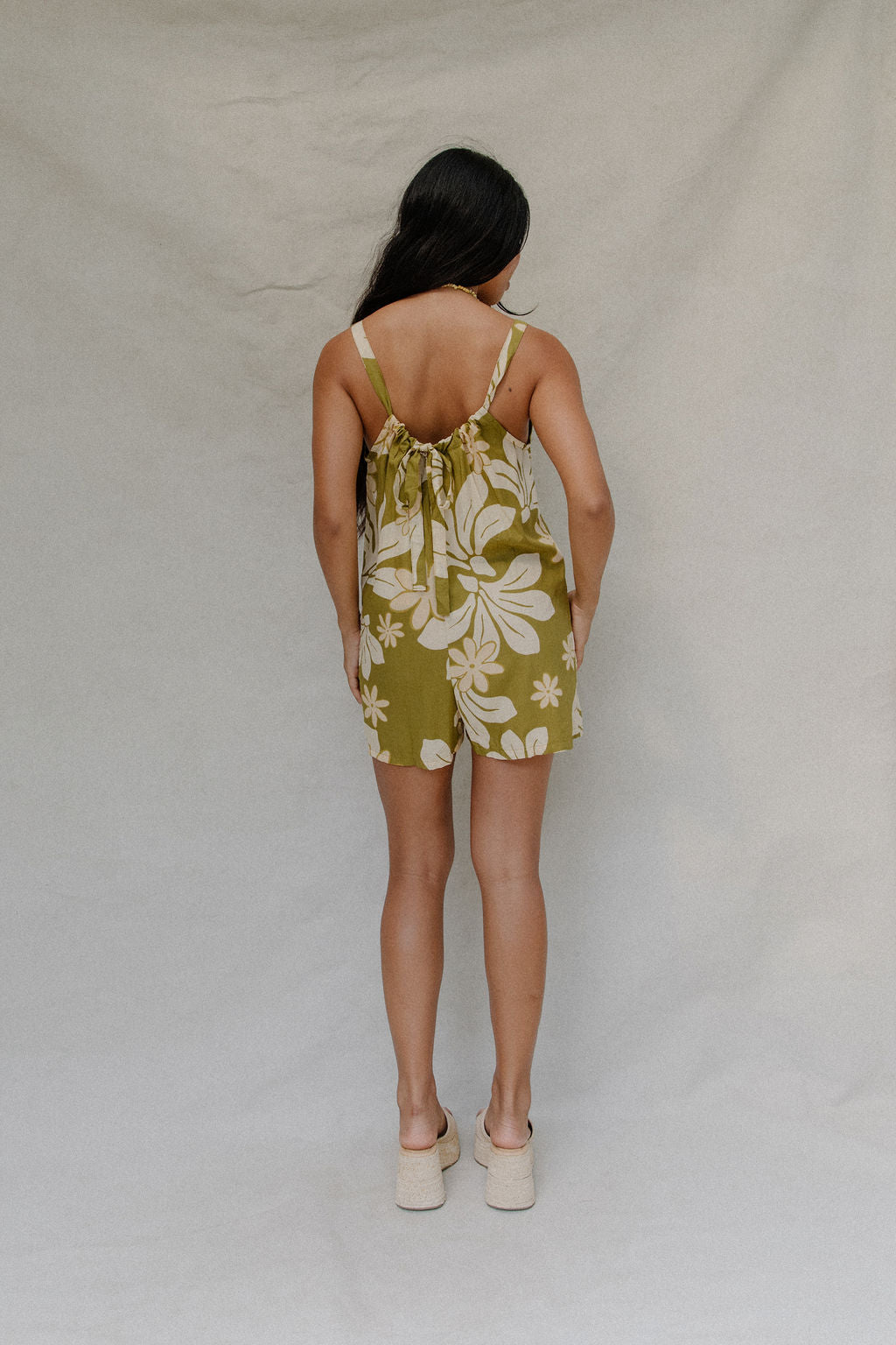 woman with brown hair wearing a green tie back romper with naupaka print