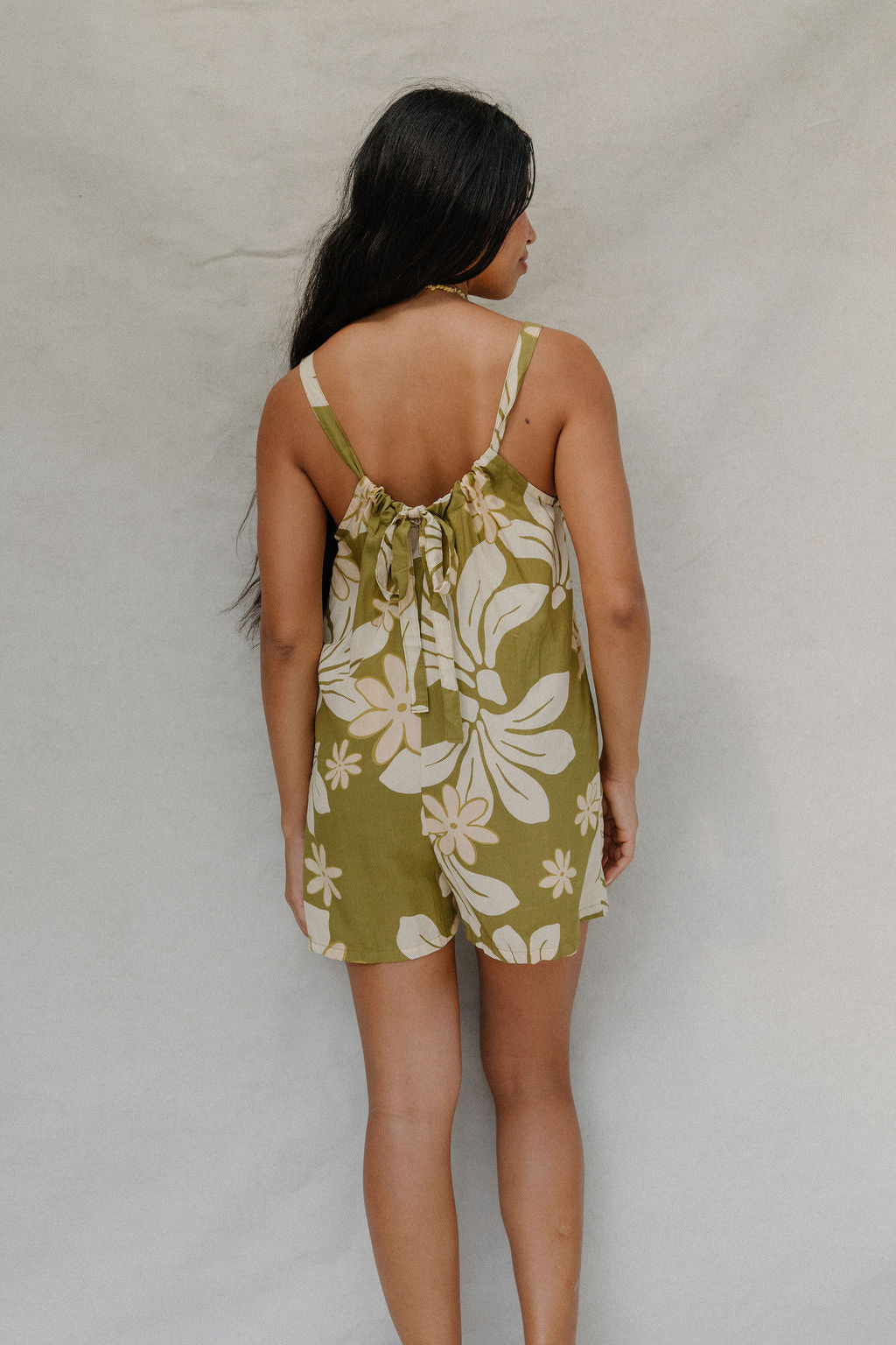 woman with brown hair wearing a green tie back romper with naupaka print