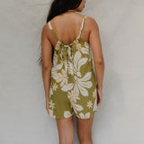 woman with brown hair wearing a green tie back romper with naupaka print
