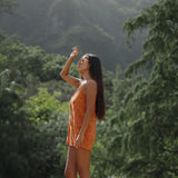 woman with brown hair wearing an orange tie back romper with puakenikeni print
