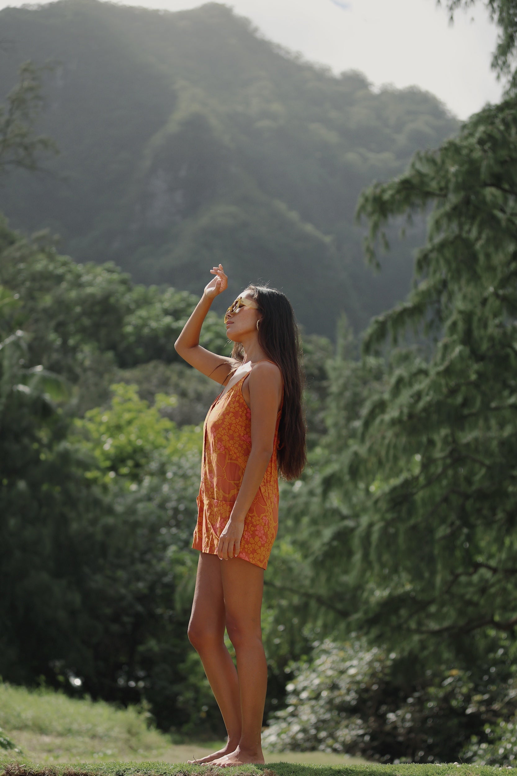 woman with brown hair wearing an orange tie back romper with puakenikeni print