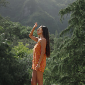 woman with brown hair wearing an orange tie back romper with puakenikeni print
