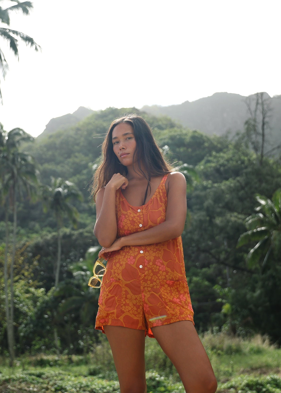 woman with brown hair wearing an orange tie back romper with puakenikeni print