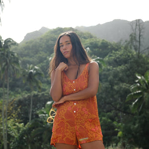 woman with brown hair wearing an orange tie back romper with puakenikeni print