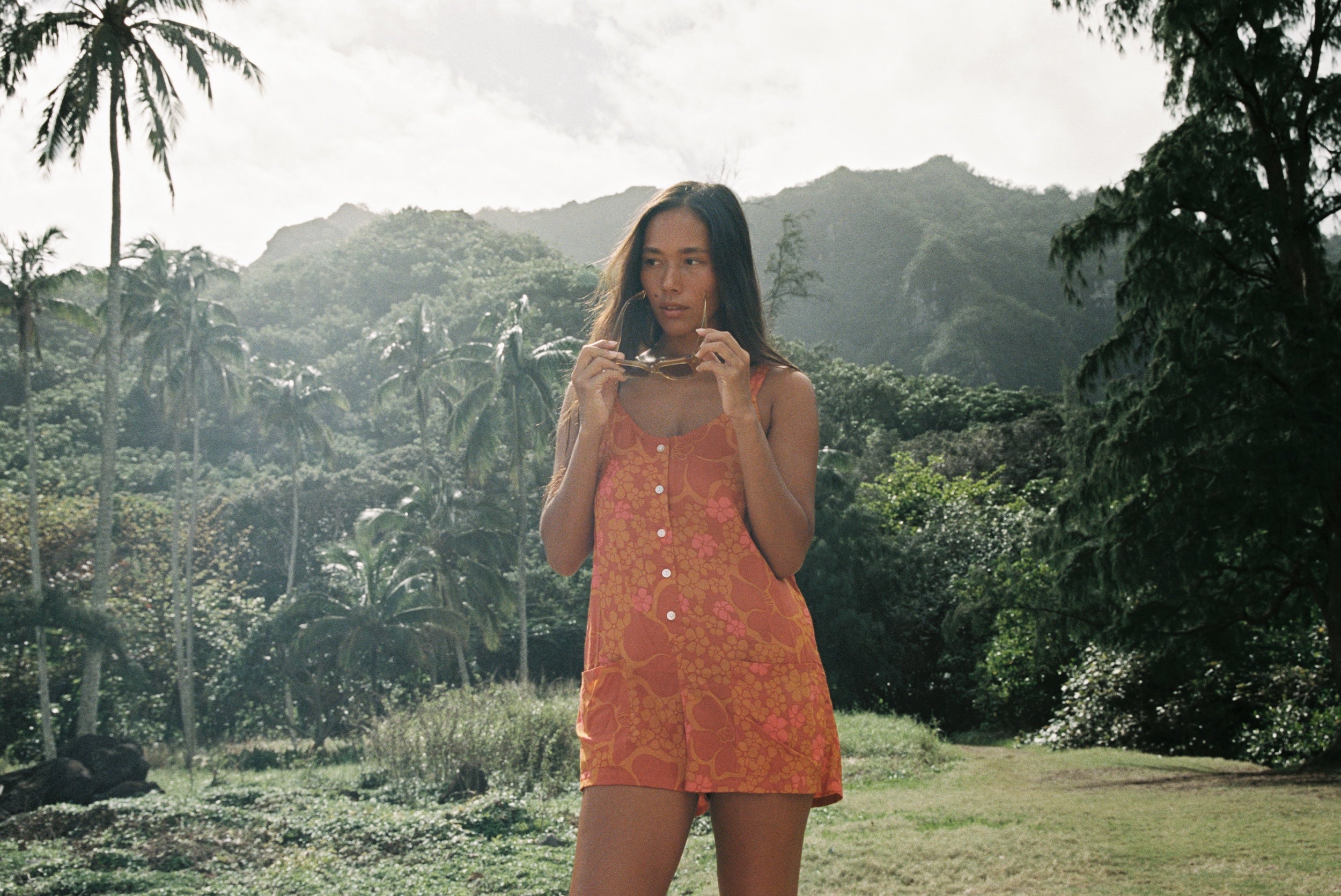 woman with brown hair wearing an orange tie back romper with puakenikeni print