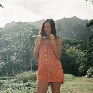 woman with brown hair wearing an orange tie back romper with puakenikeni print