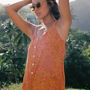 woman with brown hair wearing an orange tie back romper with puakenikeni print