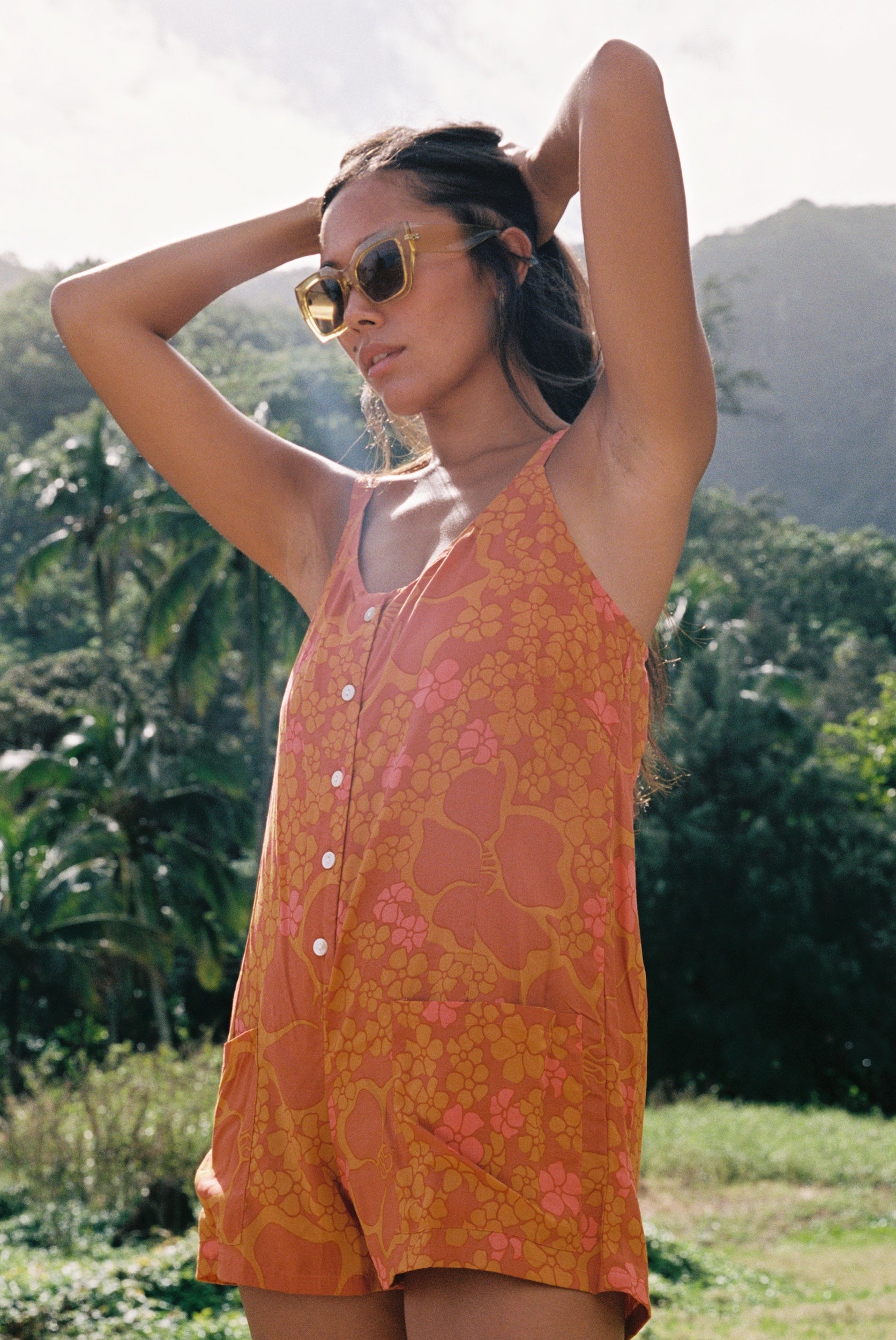 woman with brown hair wearing an orange tie back romper with puakenikeni print
