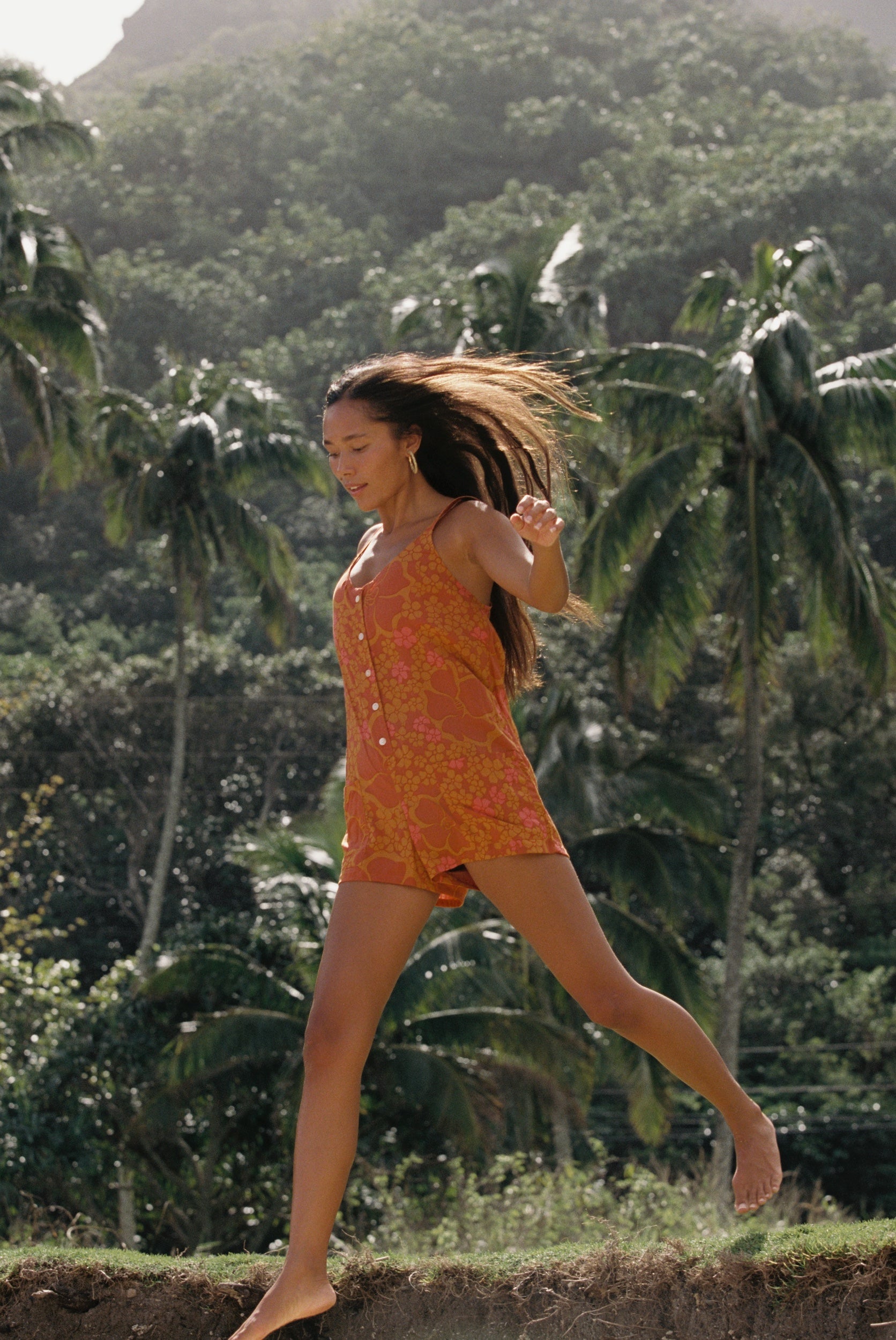 woman with brown hair wearing an orange tie back romper with puakenikeni print